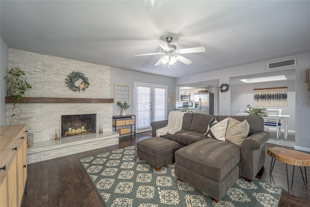 living room with ceiling fan, a stone fireplace, and dark hardwood / wood-style flooring