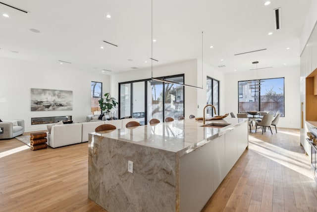 kitchen with sink, white cabinetry, a spacious island, light stone counters, and light hardwood / wood-style floors