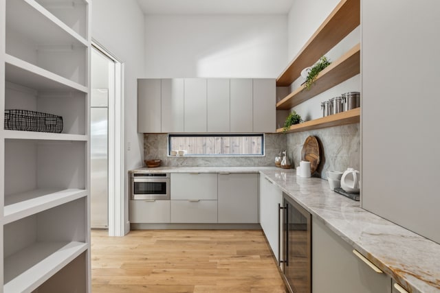 kitchen with oven, backsplash, beverage cooler, and light stone counters