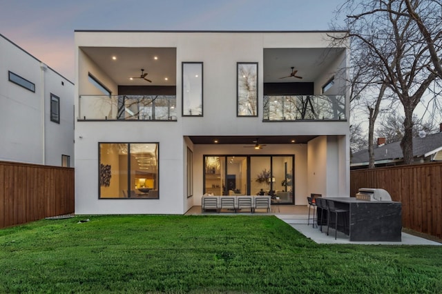 back house at dusk featuring a patio, a balcony, ceiling fan, and a bar