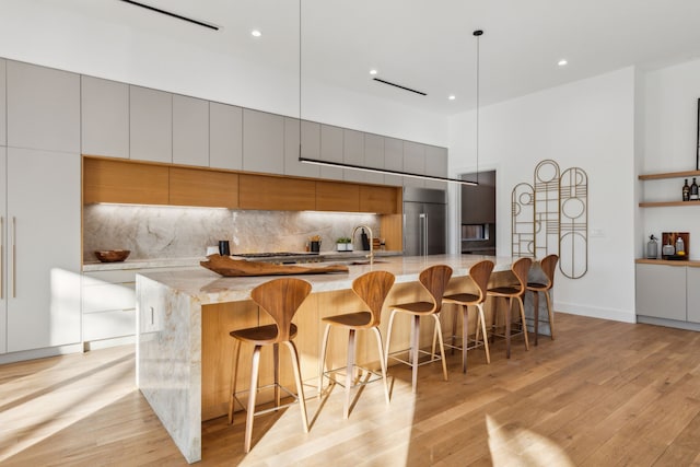 kitchen featuring decorative light fixtures, a kitchen bar, decorative backsplash, light stone countertops, and a spacious island