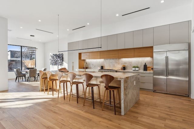 kitchen with hanging light fixtures, a kitchen breakfast bar, built in fridge, a large island, and backsplash