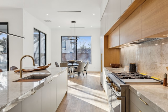 kitchen featuring sink, high end stainless steel range oven, hanging light fixtures, light stone counters, and light hardwood / wood-style flooring