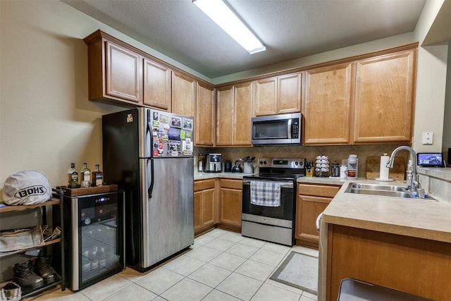 kitchen with appliances with stainless steel finishes, tasteful backsplash, sink, beverage cooler, and light tile patterned flooring