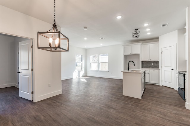 kitchen with range with electric cooktop, decorative light fixtures, sink, white cabinets, and a center island with sink