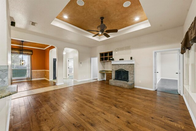 unfurnished living room with a raised ceiling, ceiling fan, hardwood / wood-style floors, and a fireplace