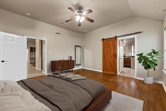 bedroom with vaulted ceiling, ensuite bath, light wood-type flooring, ceiling fan, and a barn door