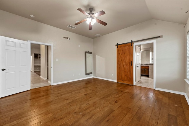 unfurnished bedroom with lofted ceiling, ensuite bathroom, light hardwood / wood-style floors, ceiling fan, and a barn door