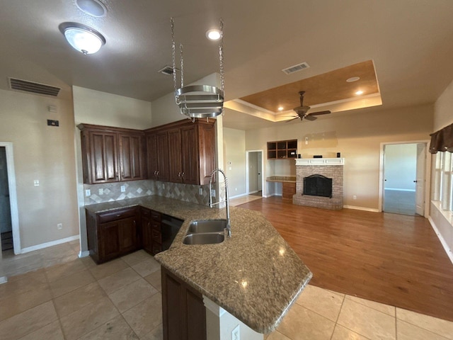 kitchen with a fireplace, sink, a raised ceiling, light stone counters, and light tile patterned flooring