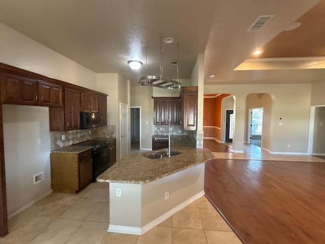 kitchen featuring light stone countertops, light tile patterned floors, stove, sink, and kitchen peninsula