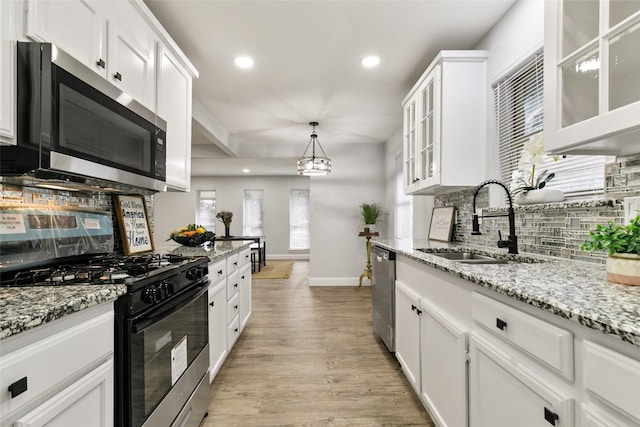 kitchen with appliances with stainless steel finishes, sink, white cabinets, pendant lighting, and backsplash