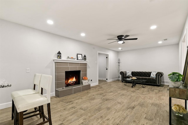 living room with ceiling fan, wood-type flooring, and a tile fireplace