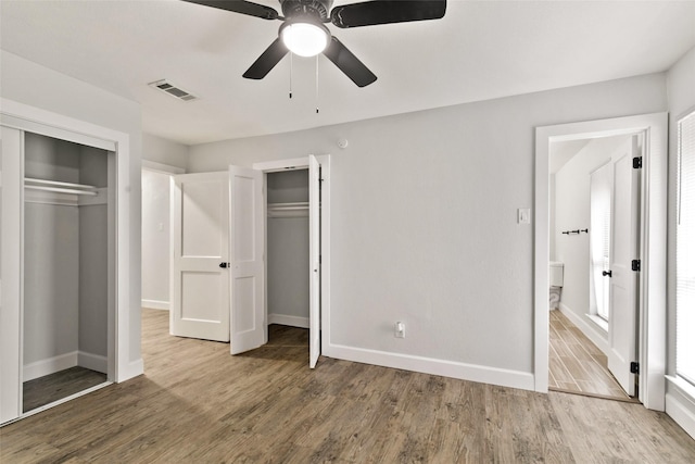 unfurnished bedroom with hardwood / wood-style flooring, two closets, and ceiling fan