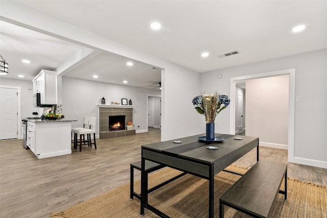 dining area featuring ceiling fan, light hardwood / wood-style flooring, and a tile fireplace