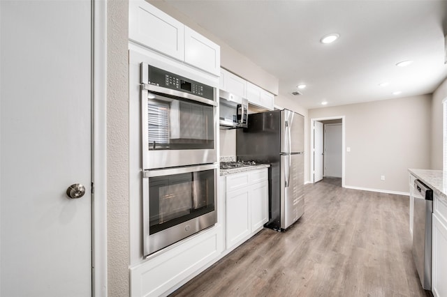 kitchen with light stone countertops, white cabinetry, appliances with stainless steel finishes, and light hardwood / wood-style flooring