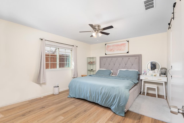 bedroom with ceiling fan, a barn door, and light hardwood / wood-style floors