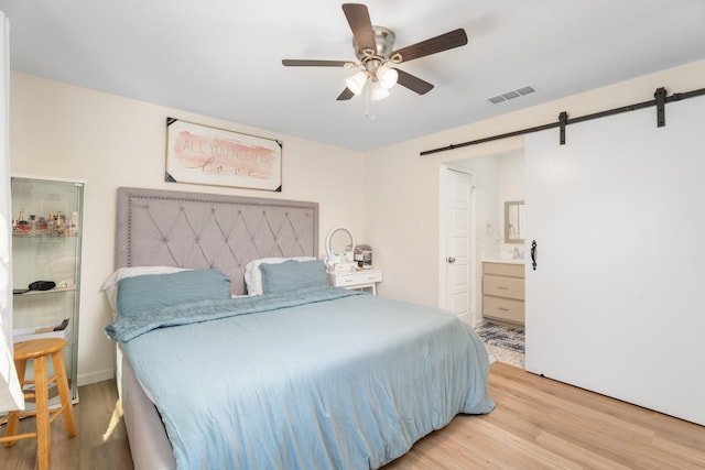 bedroom featuring ceiling fan, a barn door, ensuite bath, and light wood-type flooring