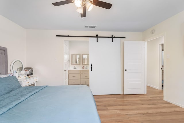 bedroom with ensuite bathroom, sink, ceiling fan, light hardwood / wood-style floors, and a barn door