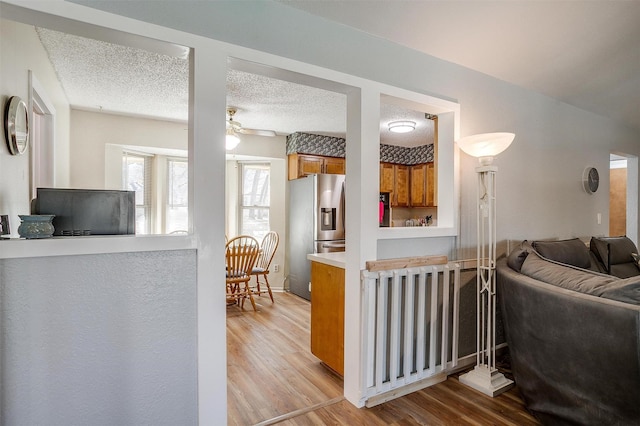 living room featuring ceiling fan, light hardwood / wood-style flooring, and a textured ceiling