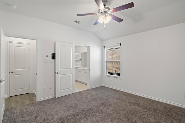 unfurnished bedroom with ceiling fan, ensuite bathroom, light carpet, and vaulted ceiling