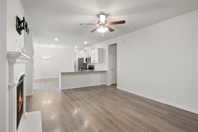 unfurnished living room featuring light wood-type flooring, ceiling fan with notable chandelier, and sink