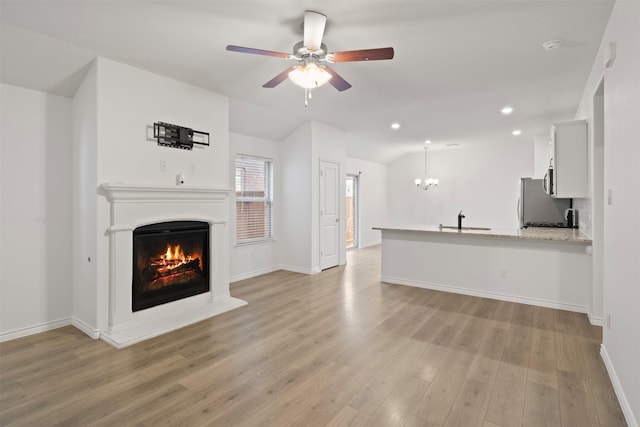 unfurnished living room with light hardwood / wood-style floors, sink, ceiling fan with notable chandelier, and vaulted ceiling