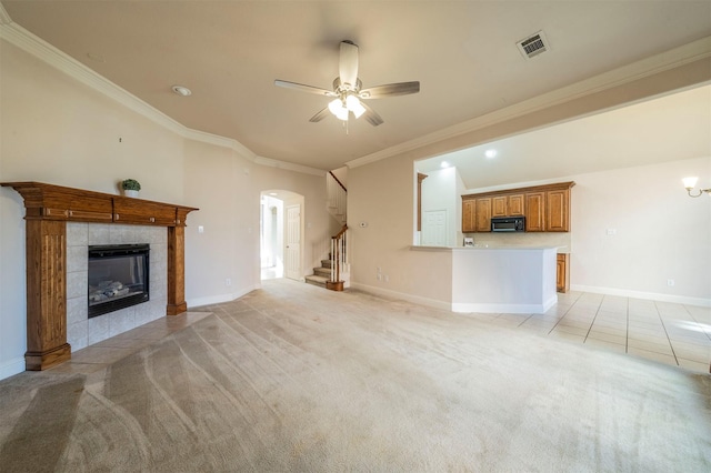 unfurnished living room featuring a tile fireplace, crown molding, light colored carpet, and ceiling fan