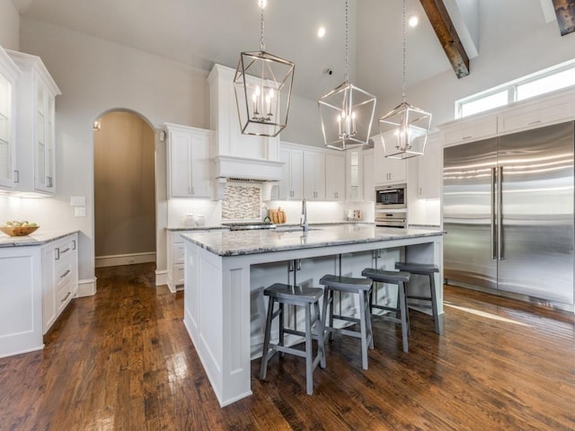 kitchen featuring white cabinets, built in appliances, backsplash, hanging light fixtures, and a large island