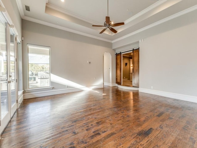 spare room featuring dark wood-type flooring, a tray ceiling, crown molding, and a barn door