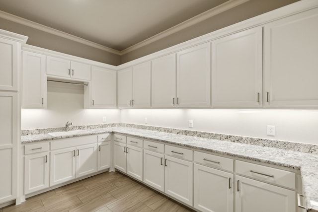 kitchen with sink, white cabinets, light stone countertops, and crown molding