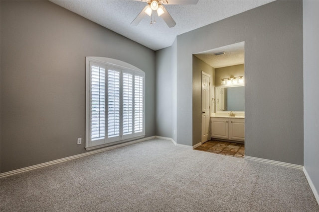 unfurnished bedroom with a textured ceiling, ensuite bath, light carpet, sink, and ceiling fan