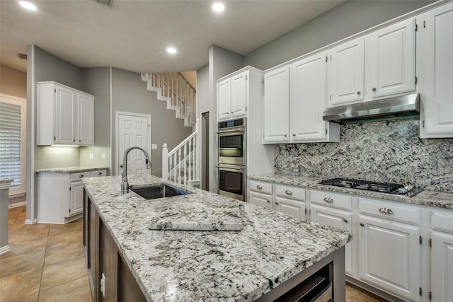 kitchen featuring sink, backsplash, white cabinetry, a center island with sink, and stainless steel appliances