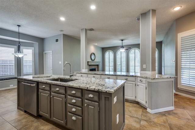 kitchen featuring a textured ceiling, decorative light fixtures, white cabinetry, sink, and a center island with sink