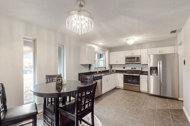 1721 Melrose St, Garland, TX 75042 - kitchen featuring stainless steel appliances, dark countertops, a chandelier, white cabinetry, and a textured ceiling