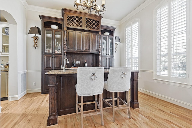 bar featuring dark brown cabinetry, crown molding, light hardwood / wood-style flooring, and light stone countertops