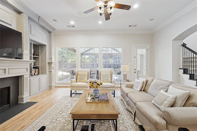 living room featuring built in shelves, light hardwood / wood-style flooring, ornamental molding, and ceiling fan