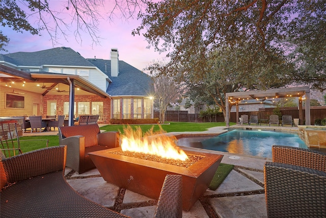 pool at dusk featuring ceiling fan, a yard, a patio, and an outdoor living space with a fire pit