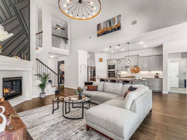 living room with a high ceiling, a brick fireplace, dark wood-type flooring, and a notable chandelier