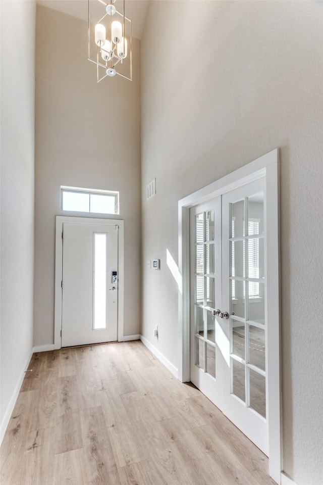 entryway featuring a towering ceiling, light hardwood / wood-style flooring, a notable chandelier, and french doors