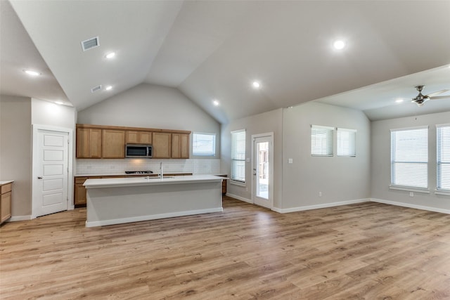 kitchen with a wealth of natural light, a kitchen island with sink, sink, and light hardwood / wood-style flooring