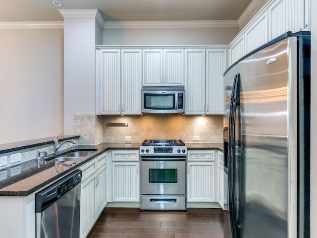 kitchen featuring white cabinets, appliances with stainless steel finishes, dark stone counters, sink, and ornamental molding