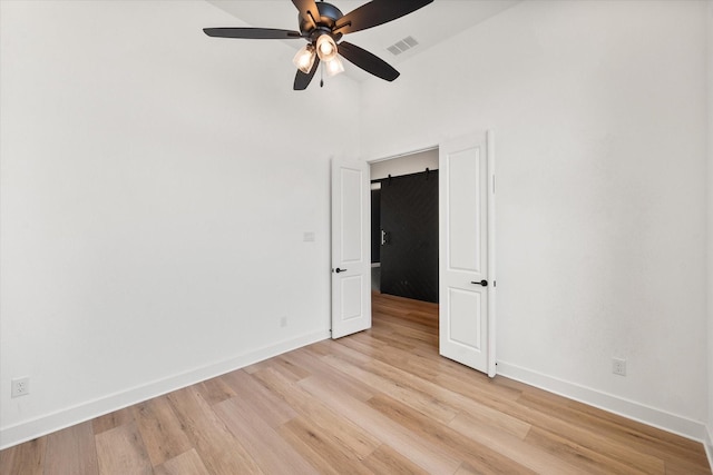 spare room with ceiling fan, a barn door, and light wood-type flooring