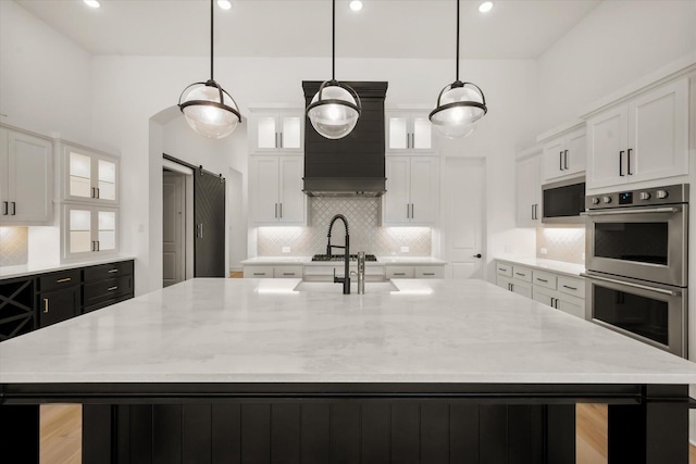 kitchen with decorative light fixtures, a barn door, white cabinets, and a center island with sink