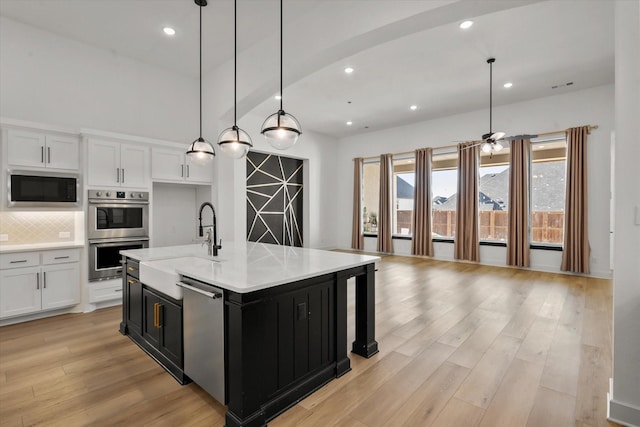 kitchen featuring appliances with stainless steel finishes, pendant lighting, white cabinetry, sink, and a kitchen island with sink