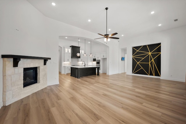 unfurnished living room with sink, a stone fireplace, light hardwood / wood-style floors, and ceiling fan