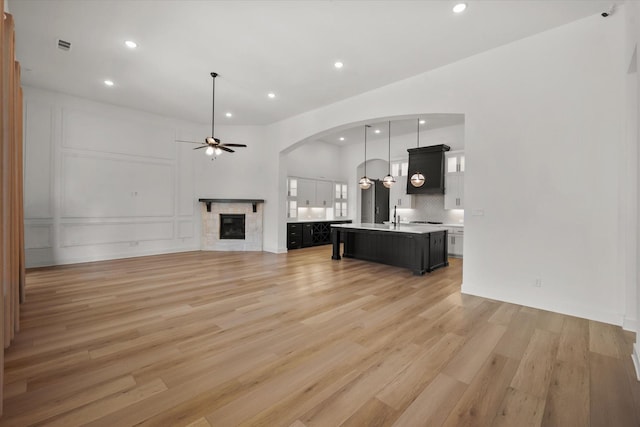 unfurnished living room with ceiling fan, sink, a stone fireplace, and hardwood / wood-style floors