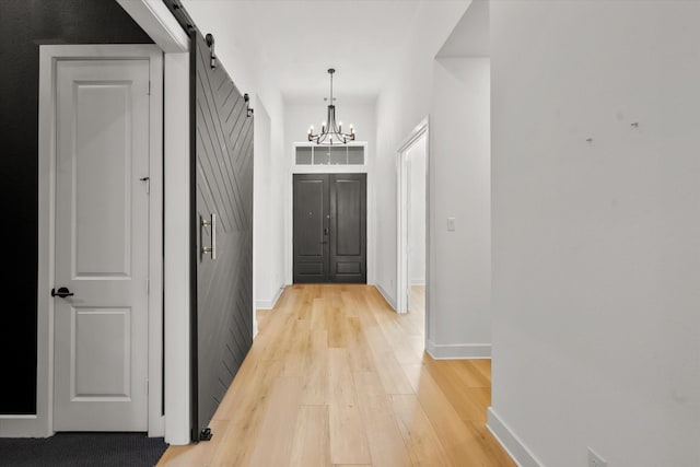 corridor with an inviting chandelier, light hardwood / wood-style floors, and a barn door