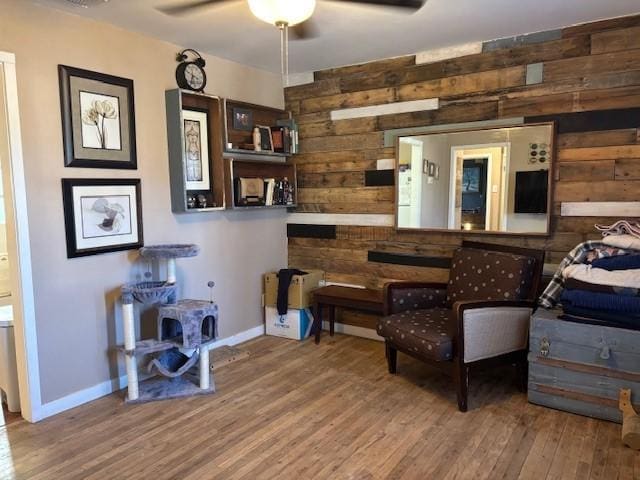 living area with wood-type flooring, wooden walls, and ceiling fan