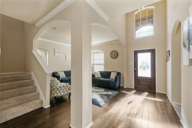 foyer featuring crown molding, plenty of natural light, dark wood-type flooring, and a towering ceiling