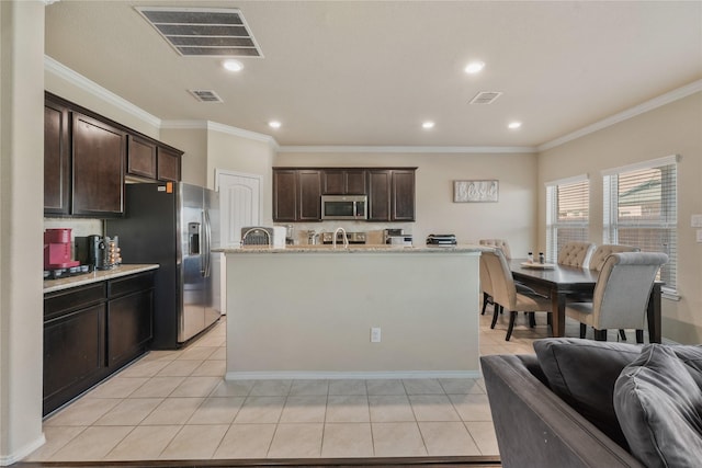 kitchen with appliances with stainless steel finishes, ornamental molding, light tile patterned floors, dark brown cabinets, and a center island with sink